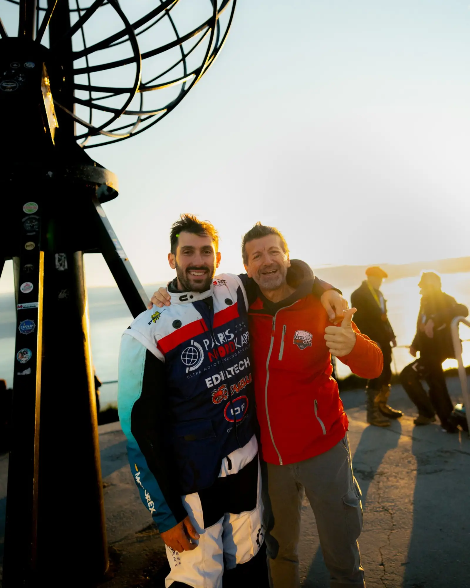 Tiziano Internò e Manuel Podetti abbracciati sotto il globo di Capo Nord, in controluce, Paris Nordkapp